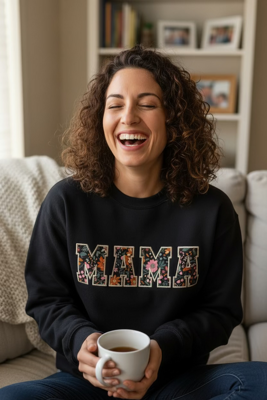 Black crewneck sweatshirt with MAMA applique letters featuring woodland creatures like foxes and deer inside embroidered outlines