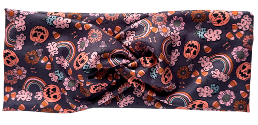 A workout headband with a twisted pattern featuring a variety of colors including pink, orange, and black, with decorative elements that give a Halloween-like appearance. The headband is displayed with a 'New' label on the top left corner.